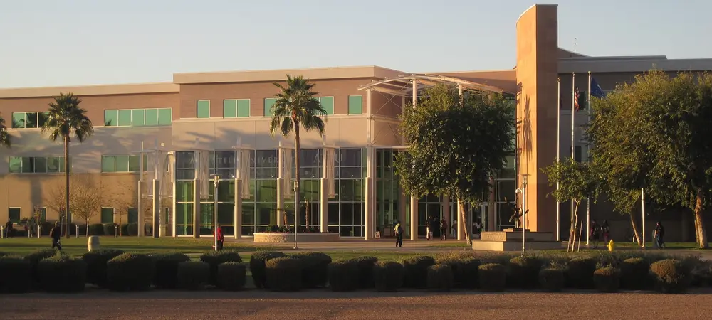 Golden-hour exterior of A.T. Still University's Mesa, Arizona campus building (glass entrance with "A.T. Still University" signage, palm trees, landscaped courtyard) — the same Mesa campus that hosts the Arizona School of Dentistry and Oral Health.