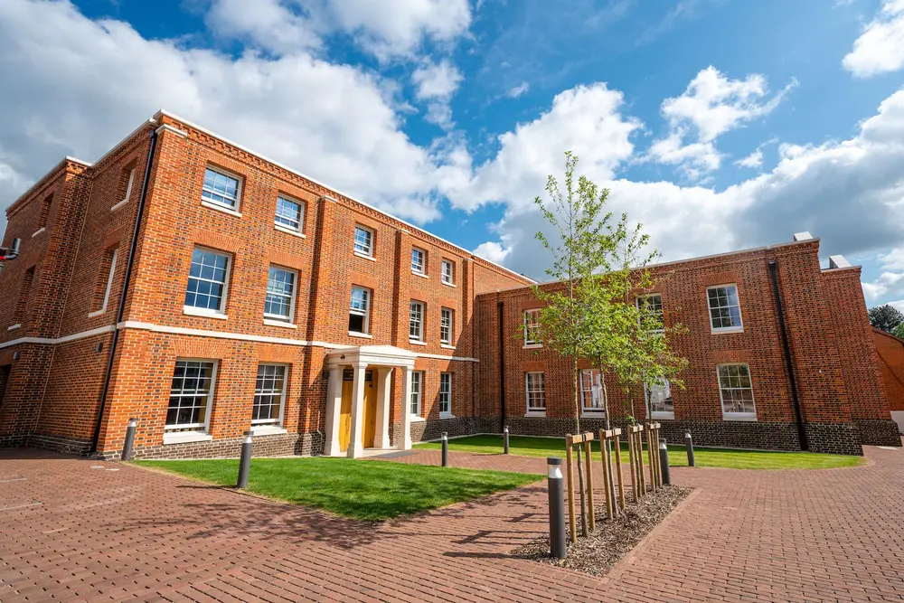The Vinson Building, University of Buckingham — red-brick campus building with a bright blue cloudy sky and green lawn