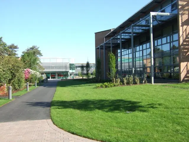 Modern glass campus building (LINC, with Health and Education faculties beyond) at Edge Hill University, Ormskirk, with green lawn and blue sky