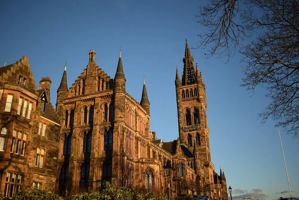 The Gilbert Scott Building (main building) and bell tower of the University of Glasgow, warm daytime light against a clear blue sky