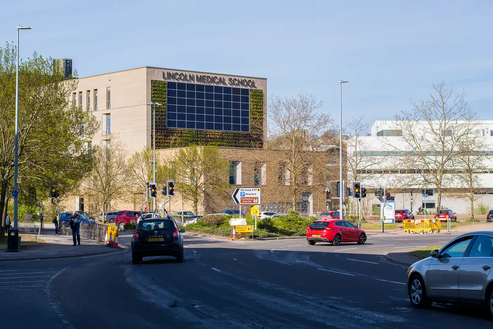 The Lincoln Medical School building at the University of Lincoln, with its distinctive green living wall and solar-panel array, under a clear blue sky.
