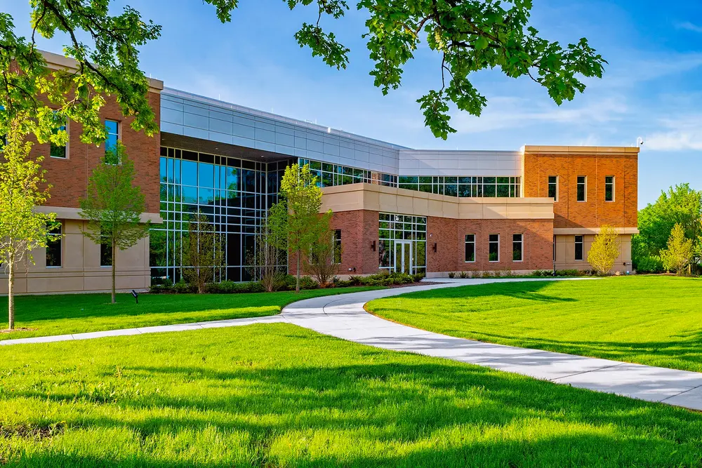 White Oak Hall, a modern brick-and-glass academic building on Midwestern University's Downers Grove, Illinois campus (host campus of the College of Dental Medicine Illinois), on a clear day with green lawn and curving walkway.