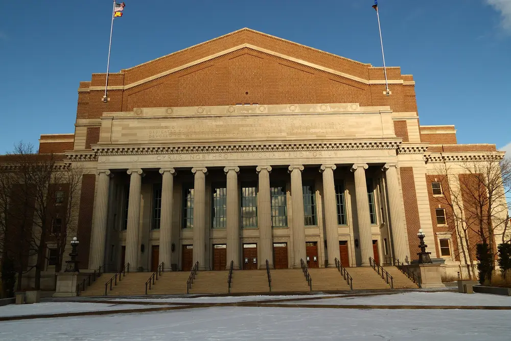The iconic columned neoclassical facade of Cyrus Northrop Memorial Auditorium, the flagship building of the University of Minnesota (parent of its School of Dentistry) in Minneapolis, under a clear blue sky.
