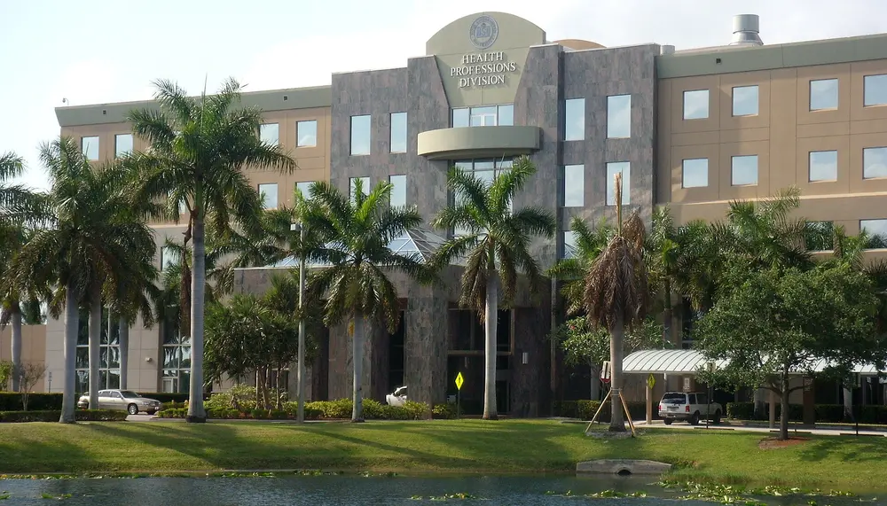 Exterior of Nova Southeastern University's Health Professions Division building (Davie/Fort Lauderdale, FL), the complex that houses the College of Dental Medicine; daytime front facade with royal palms and reflecting pond.