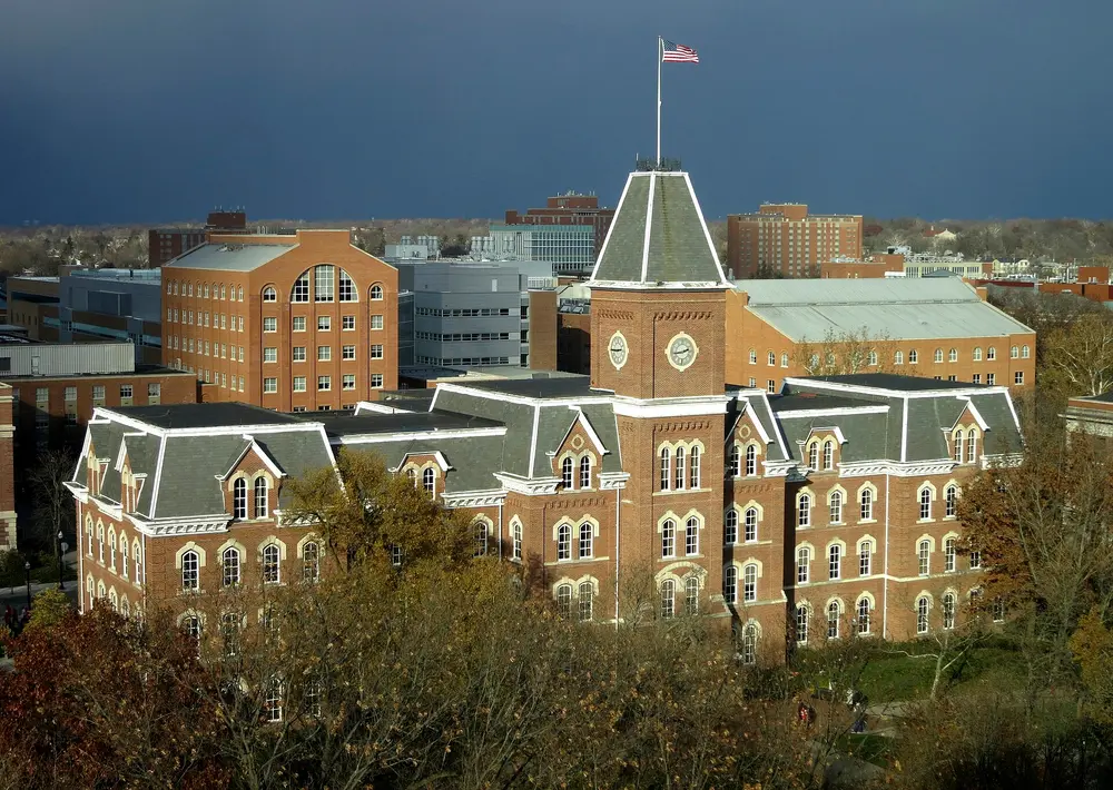 University Hall, the iconic red-brick main building with clock tower and US flag on the Oval at The Ohio State University, Columbus, OH — the parent institution of the College of Dentistry.