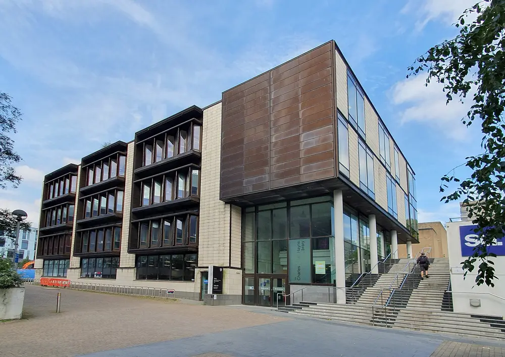 The Charles Seale-Hayne Library, a flagship modern building on the main University of Plymouth city-centre campus (host university of the Peninsula Dental School), Plymouth, Devon, UK — copper-clad cube and glass facade under a clear blue sky.