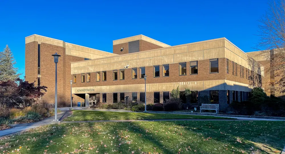 The Administration Building at Stony Brook University (SUNY), the host institution of the School of Dental Medicine, in Stony Brook, NY — a clean daytime exterior with blue sky and green lawn.
