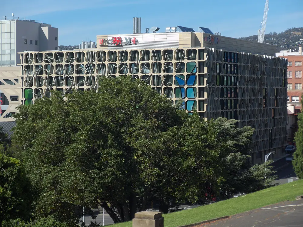The University of Tasmania Medical Sciences building (MS2) in Hobart, the home of UTAS medicine, with its distinctive perforated concrete facade and UTAS signage against a clear blue sky.