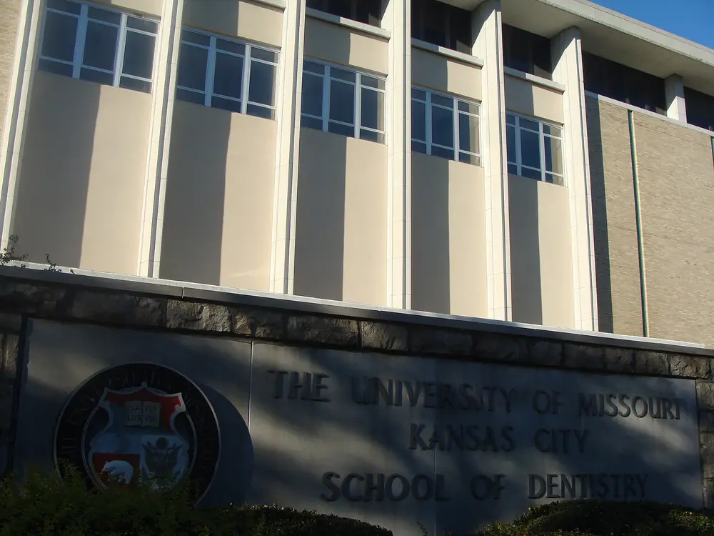 Daytime exterior of the University of Missouri-Kansas City School of Dentistry building on the Health Sciences (Hospital Hill) campus, with the engraved stone monument and university seal identifying the school.