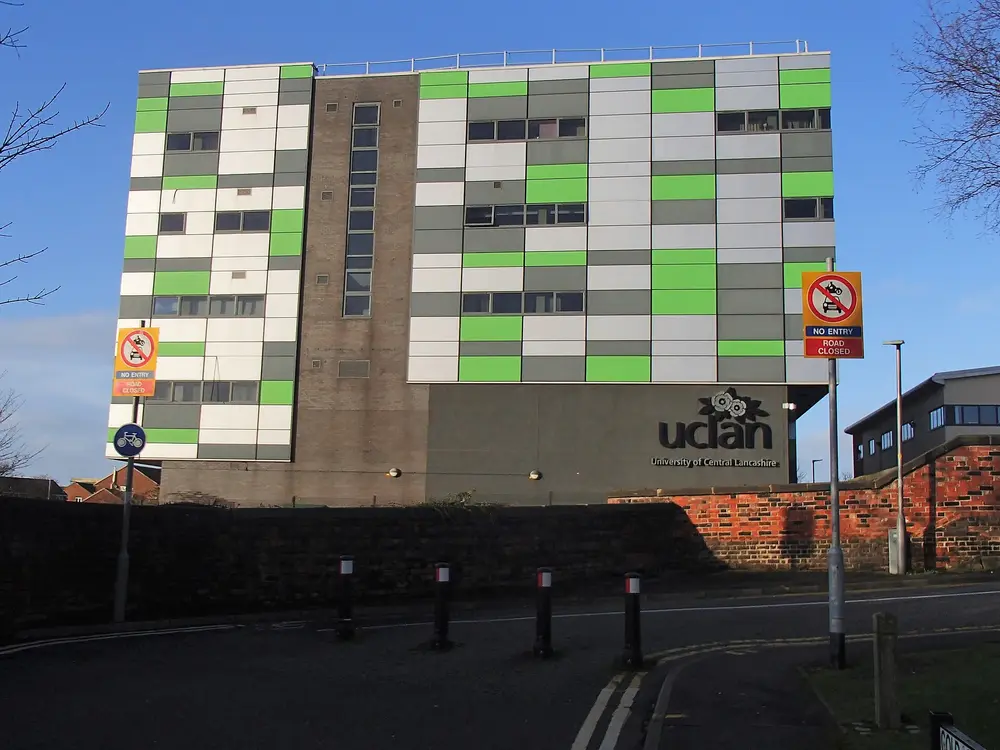 The Media Factory, University of Central Lancashire, Preston — modern green/grey/white clad campus building under a clear blue sky, with the "uclan / University of Central Lancashire" branding on the facade