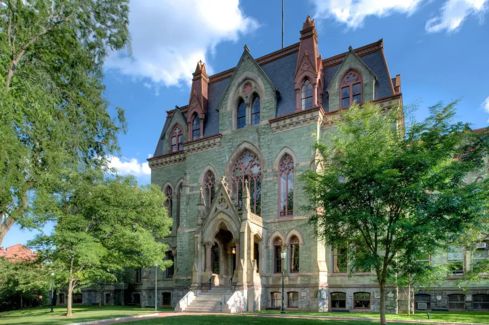 College Hall, the iconic Gothic flagship building of the University of Pennsylvania (host university of Penn Dental Medicine) in Philadelphia, PA — sunlit daytime facade with blue sky and green trees.